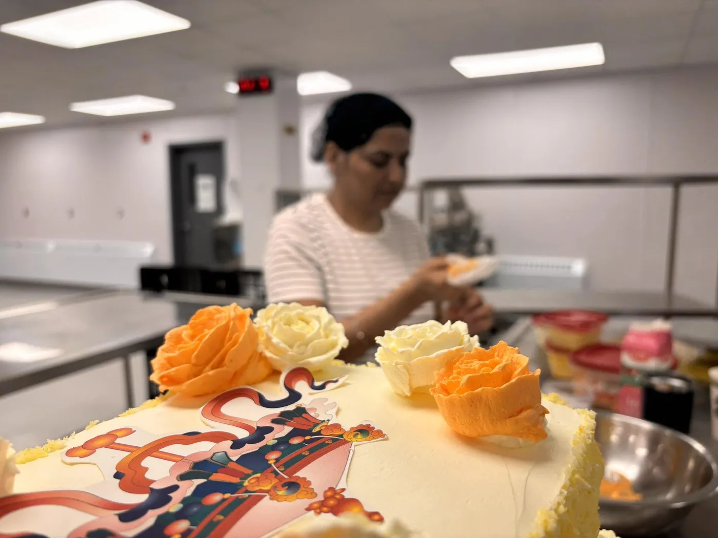 Harpreet decorating a custom cake with buttercream roses in the bakery kitchen